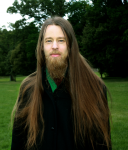 Halvkroppsbild på Rasmus som står i en grön park och ser in i kameran