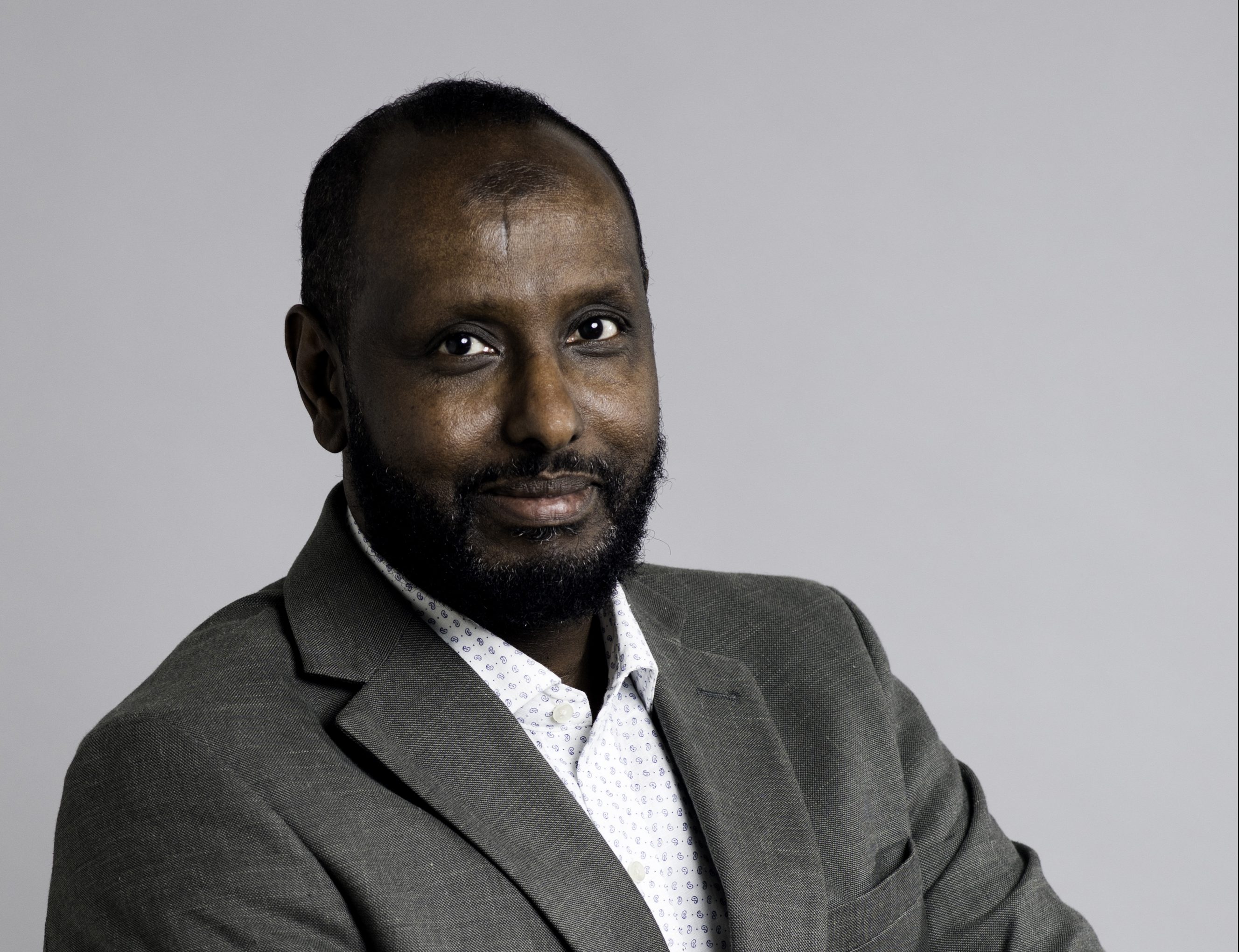 Rashid Mohammed, halvkropp i grå kavaj och vit skjorta mot vit bakgrund. Foto Jessica Segerberg