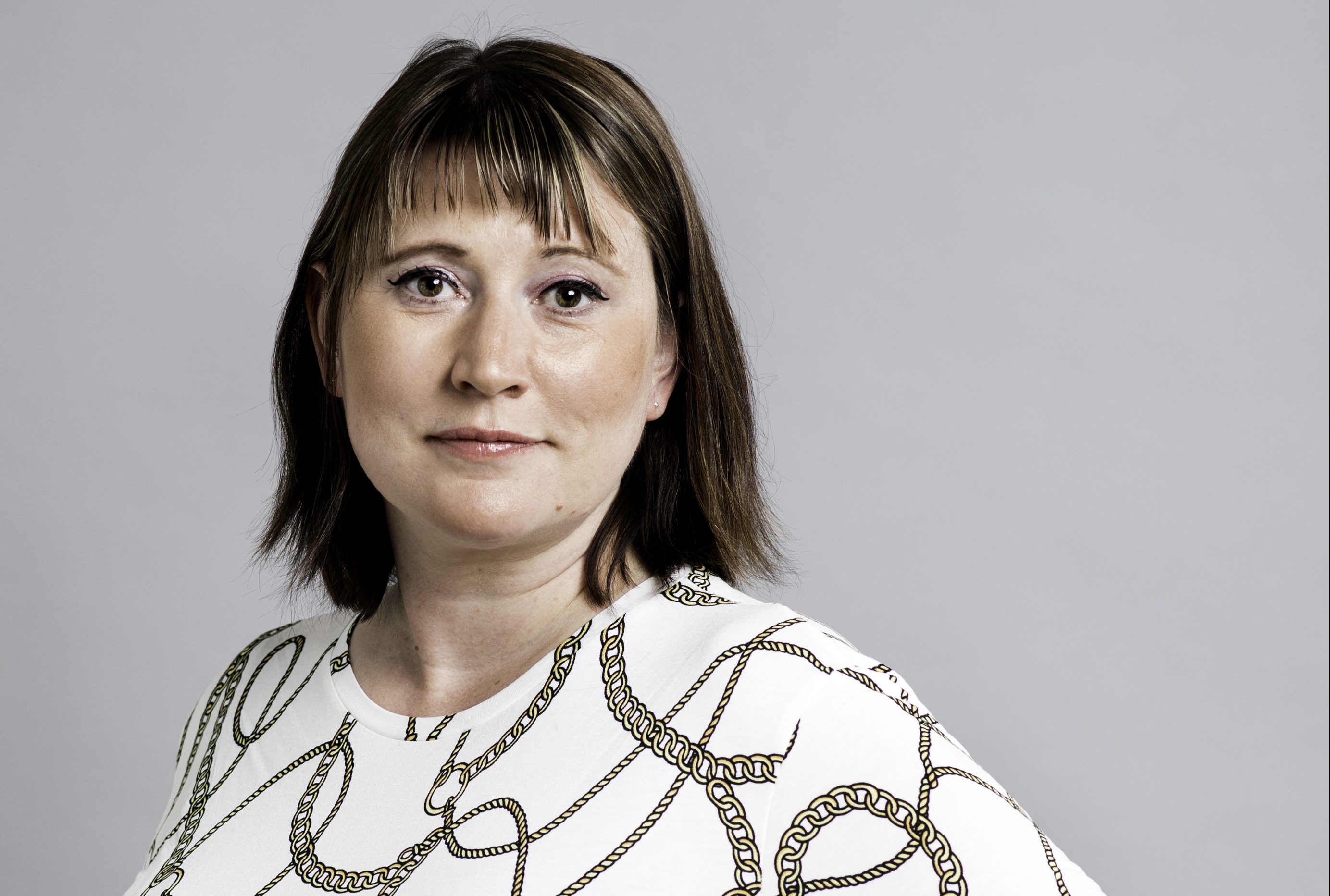 Sara Stenudd, halvkropp i vit mönstrad tröja mot vit bakgrund. Foto Jessica Segerberg