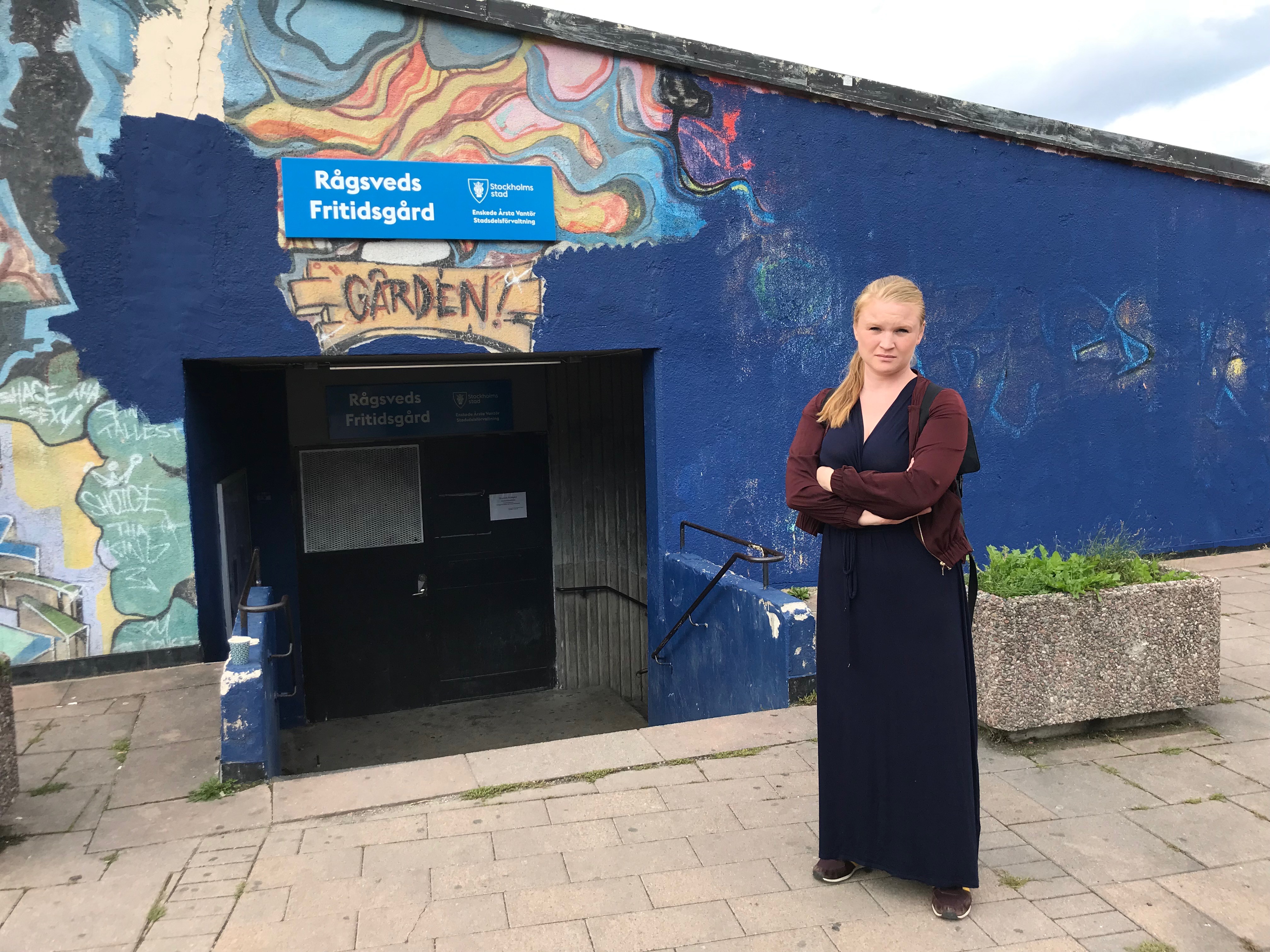 Clara Lindblom står framför den delvis övermålade graffitiväggen i Rågsveds centrum