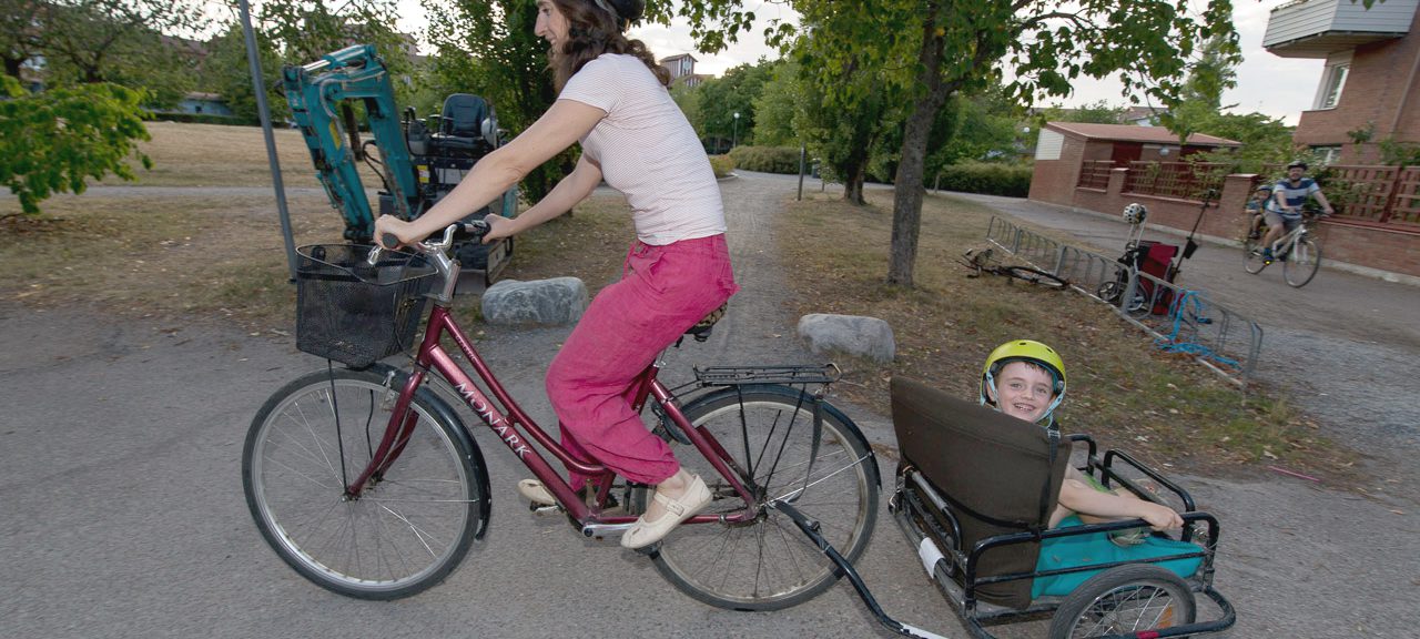 Kvinna cyklar med barn i cykelvagn.