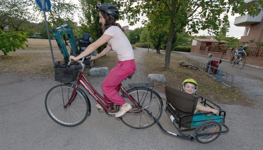 Kvinna cyklar med barn i cykelvagn.