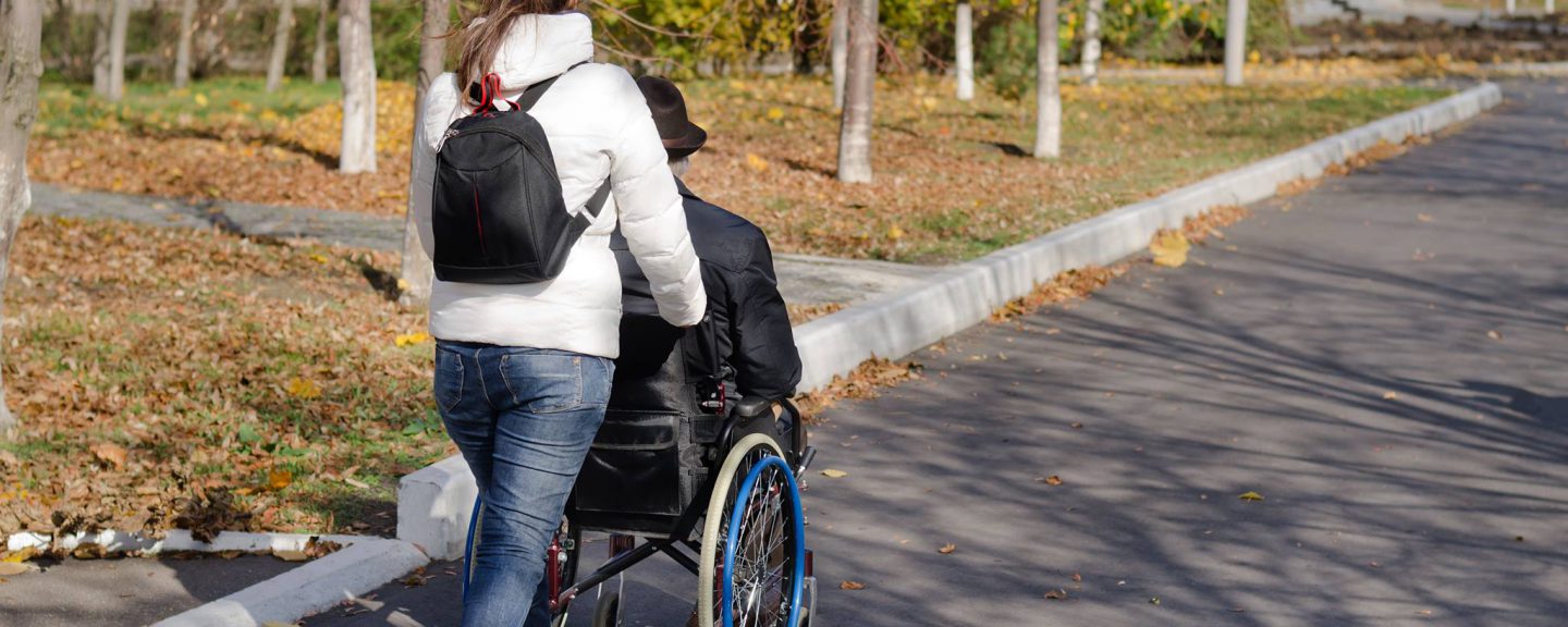 Ung personal som skjutsar äldre person i rullstol, vårmiljö.