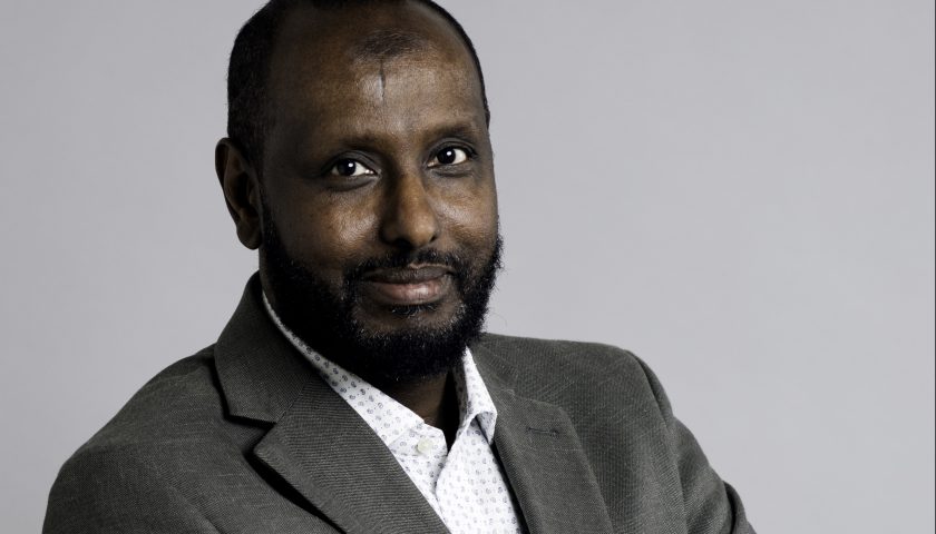 Rashid Mohammed, halvkropp i grå kavaj och vit skjorta mot vit bakgrund. Foto Jessica Segerberg